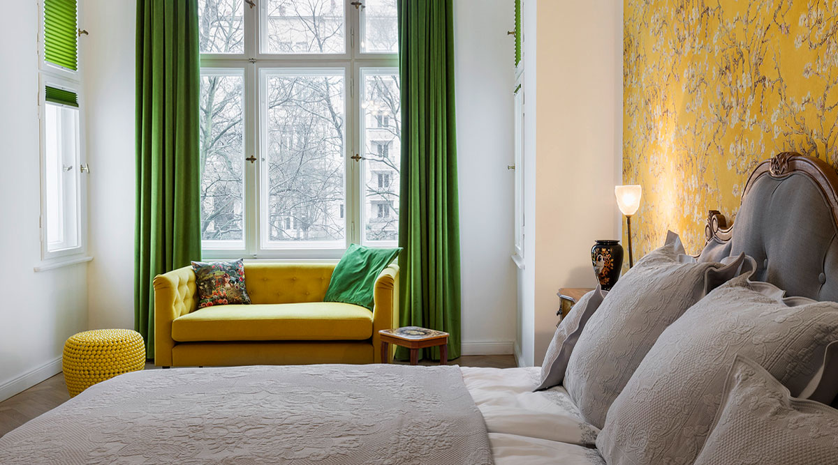 Schlafzimmer mit Van Gogh Tapete, gelbes Sofa vor grünen Samtvorhängen